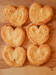 Delicate cookies made in heart shape on wooden board underneath. French style pastry sweet desert. Bakery product. Selective focus. Warm color. Tasty treat for tea or coffee
