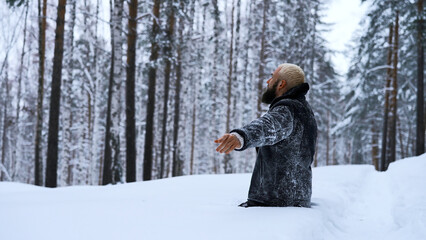 Happy young man in fairytale winter forest praying to god standing on his knees. Media. Concept of religion and feeling unity with nature.