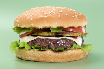 Burger with delicious patty on green background, closeup