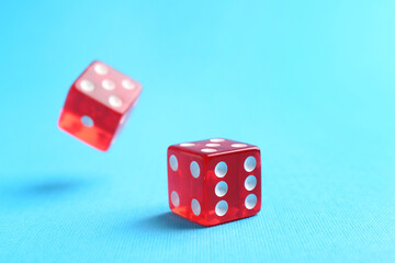 Two red game dices falling on light blue background, closeup
