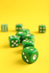 Many green game dices on yellow background, closeup