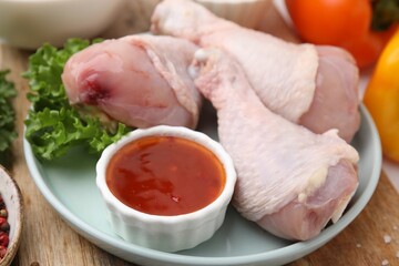Fresh marinade, raw chicken drumsticks and lettuce on wooden table, closeup