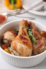 Delicious roasted chicken drumsticks with rosemary and tomatoes in bowl on white table, closeup