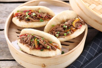 Delicious gua bao in bamboo steamer on wooden table, closeup