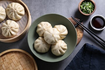 Delicious bao buns (baozi), chopsticks, soy sauce and green onion on grey table, flat lay