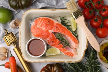 Fresh fish, lime, rosemary and marinade in baking dish surrounded by products on light table, flat...
