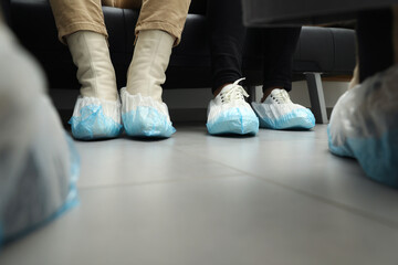 Women wearing blue shoe covers onto different footwear indoors, closeup