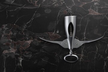One wing corkscrew on black marble table, top view. Space for text
