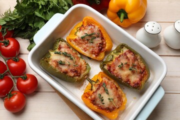 Tasty stuffed peppers in dish and ingredients on wooden table, flat lay