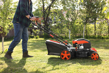 Man cutting green grass with lawn mower in garden, closeup