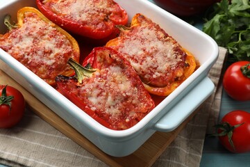 Tasty stuffed peppers in dish and ingredients on light blue wooden table, closeup