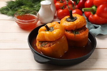 Tasty stuffed peppers in pan, sauce and products on light wooden table, closeup