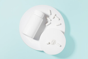 White mockup jar and pills or capsules on white pedestal on blue isolated background. The concept of dietary supplements, pharmacy and medicine for the treatment of diseases