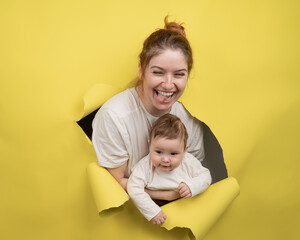 Cheerful Caucasian woman with little son rips and leans out through yellow cardboard background. 