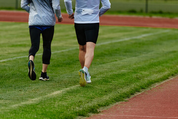 An inspiring and active elderly couple showcase their dedication to fitness as they running together on a lush green field, captured in a close-up shot of their legs in motion.