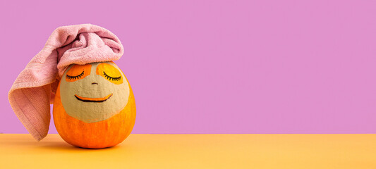Pumpkin with clay mask and towel on table against lilac background