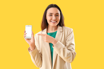 Happy young woman with smartphone on yellow background
