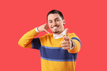 Cool young man showing "call me" gesture and pointing at viewer on red background