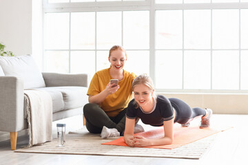 Sporty young woman helping her friend to do exercise at home