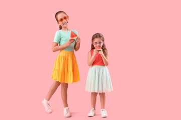 Happy little girls with slices of fresh watermelon on pink background