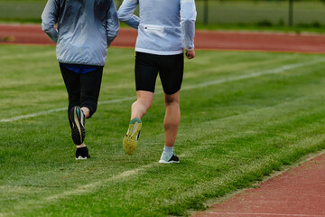 An inspiring and active elderly couple showcase their dedication to fitness as they running together on a lush green field, captured in a close-up shot of their legs in motion.