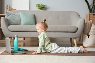 Cute little girl practicing yoga on mat while watching online tutorial in living room