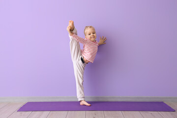 Cute little girl practicing yoga on mat against lilac background