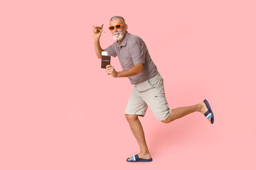 Mature man with passport and wooden airplane running on pink background. Travel concept