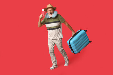 Shocked mature man with passport and suitcase on red background. Travel concept