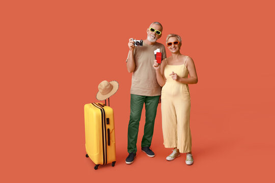 Mature couple with travel accessories and suitcase on orange background
