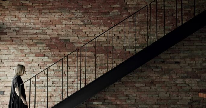 Old brick wall of brown color in a modern apartment with black stair, The woman was climbing the stairs in the house to the second floor of the house. textured surface, wall with modern stair.