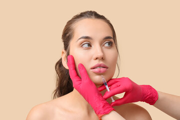 Young woman receiving lip injection against color background