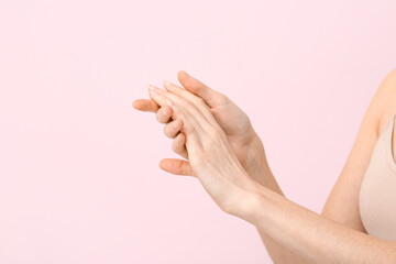 Young woman applying hand cream on pink background