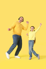 Fototapeta premium Father and his daughter in headphones listening to music and dancing on yellow background