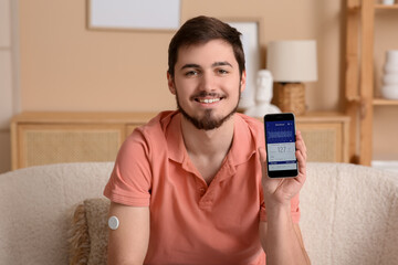 Diabetic young man with glucose sensor and mobile phone measuring blood sugar level at home