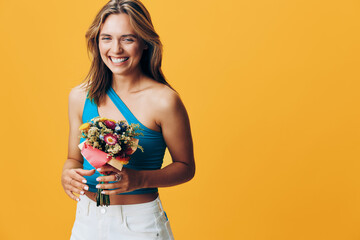 Happy woman holding a colorful bouquet of flowers in front of a vibrant yellow background with a...