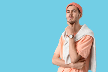 Handsome young man in stylish peach t-shirt and hat posing on blue background