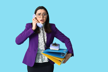 Stressed businesswoman with folders and telephone on blue background