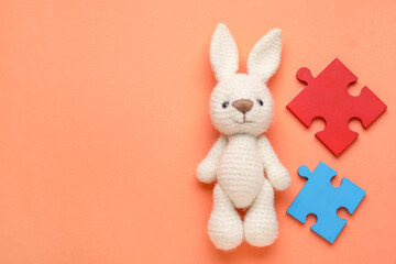 Colorful puzzle pieces and toy bunny on orange background. Concept of autistic disorder. Top view