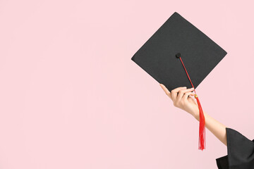 Female hand with graduation hat on pink background