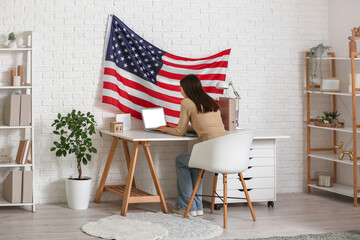 Young woman using laptop at workspace with USA flag on wall