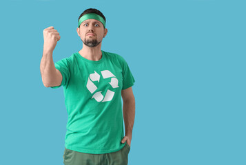 Angry young man in t-shirt with recycling logo shaking fist on blue background. Ecology concept