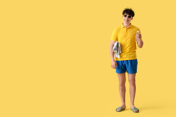 Fototapeta premium Handsome young happy man with beach blanket and bottle of water on yellow background