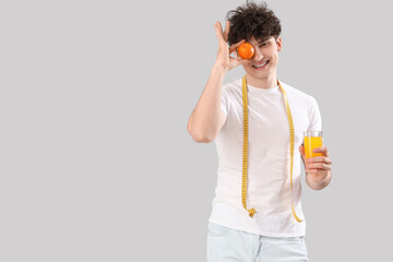 Handsome young happy sporty man with measuring tape, glass of juice and orange on grey background. Weight loss concept