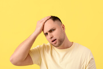 Worried young man with hair loss problem on yellow background, closeup