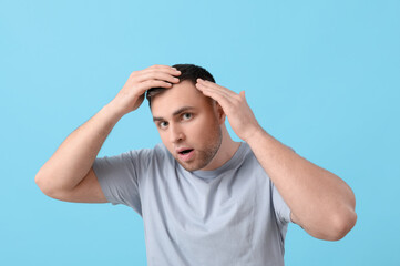 Shocked young man with hair loss problem on blue background