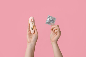 Female hands with vibrator and condom on pink background, closeup