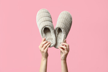 Female hands holding grey slippers on pink background