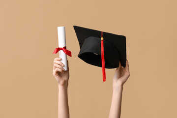 Female hands with graduation hat and diploma on beige background