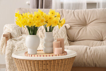 Comfortable sofa, coffee table with candles and bouquets of narcissus flowers in living room